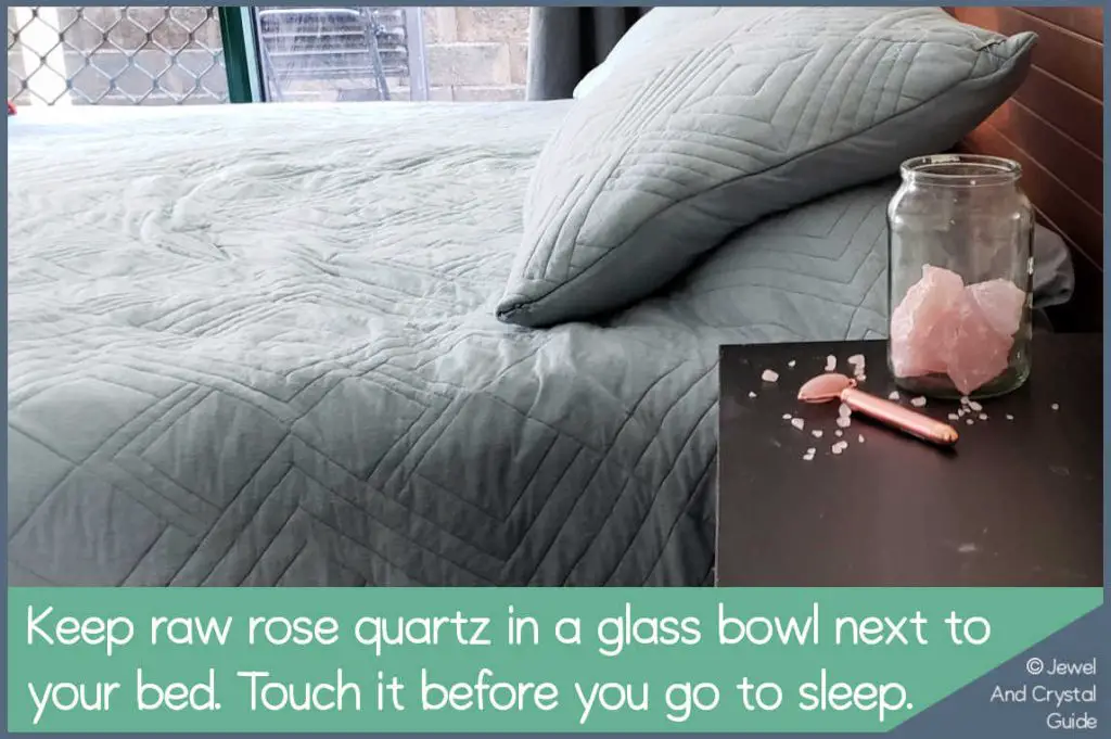 Photo of a bowl of raw rose quartz next to a bed
