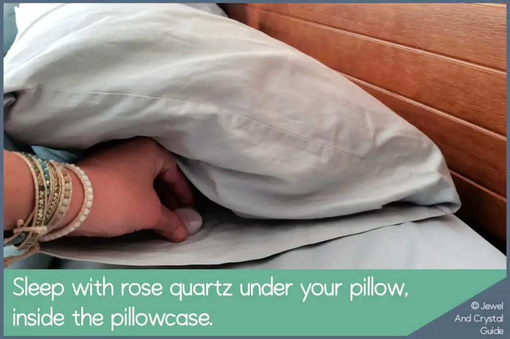 Photo of a hand placing rose quartz under a pillow inside a pillowcase