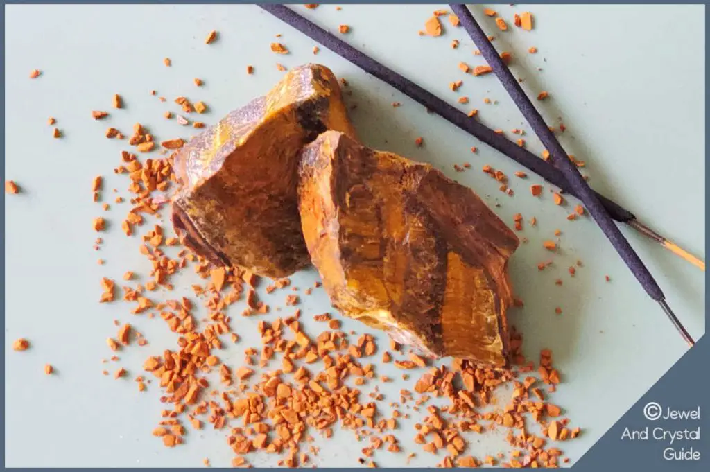 Photo of tiger's eye crystal lying next to incense sticks and in grains of sand