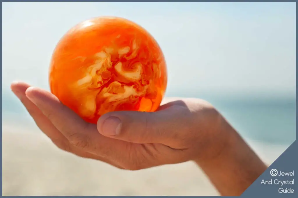 Photo of hand holding a ball of amber with the Baltic sea n the background