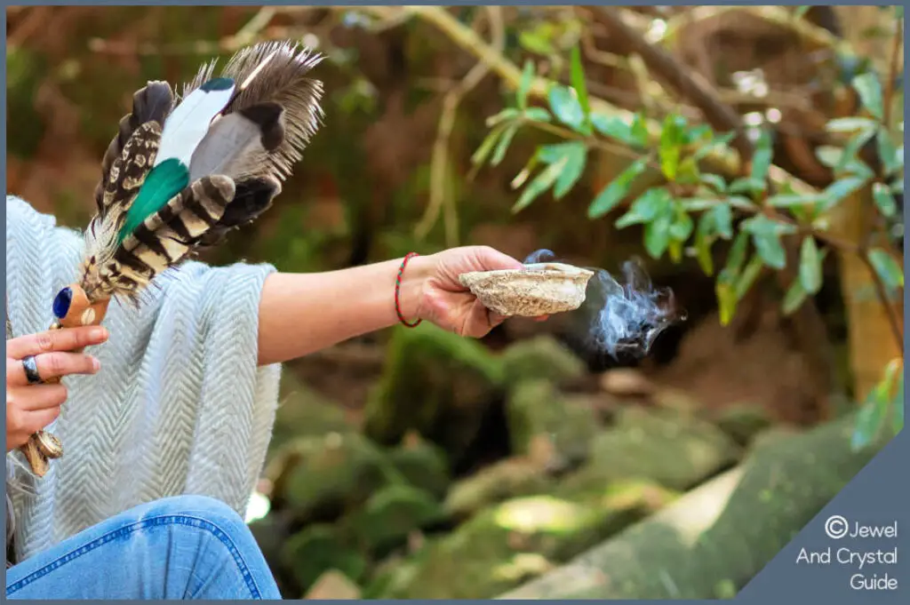 Woman cleansing amazonite out in nature with feathers, a smudge stick, and a seashell